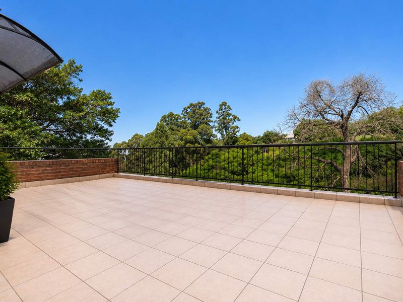 Spacious outdoor balcony featuring tiled flooring, a secure metal balustrade, and a brick parapet wall, offering elevated views of the surrounding greenery.