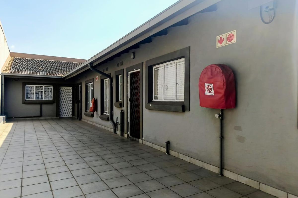 A paved exterior walkway area featuring security gates, fire safety equipment, and tiled flooring along the side of the apartment building.