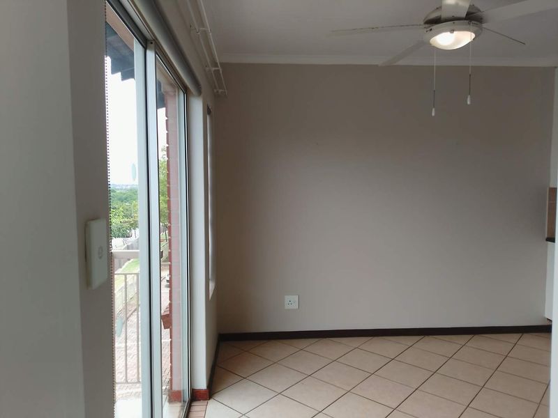 An empty open-plan living area featuring tiled floors, a ceiling fan, and large sliding glass doors leading to an outdoor space.