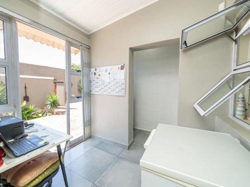 A functional laundry or utility space featuring tiled flooring, aluminium window frames, and direct access to the rear garden area.