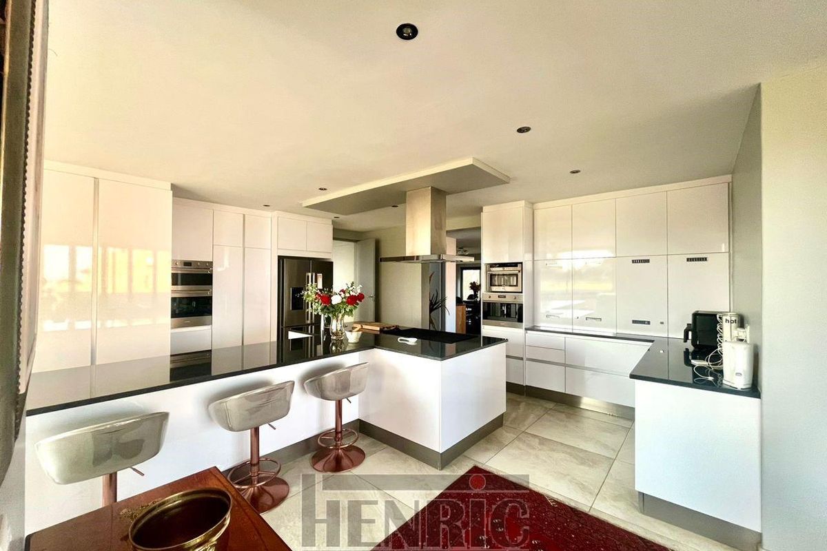 Modern kitchen featuring high-gloss white cabinetry, black stone countertops, a central island with breakfast bar, and integrated stainless steel appliances.