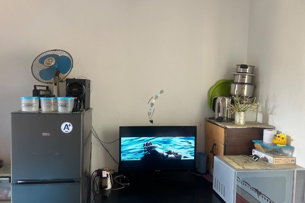 A functional utility corner featuring a compact refrigerator, microwave, and television setup, providing essential kitchen and media utility in a compact living space.