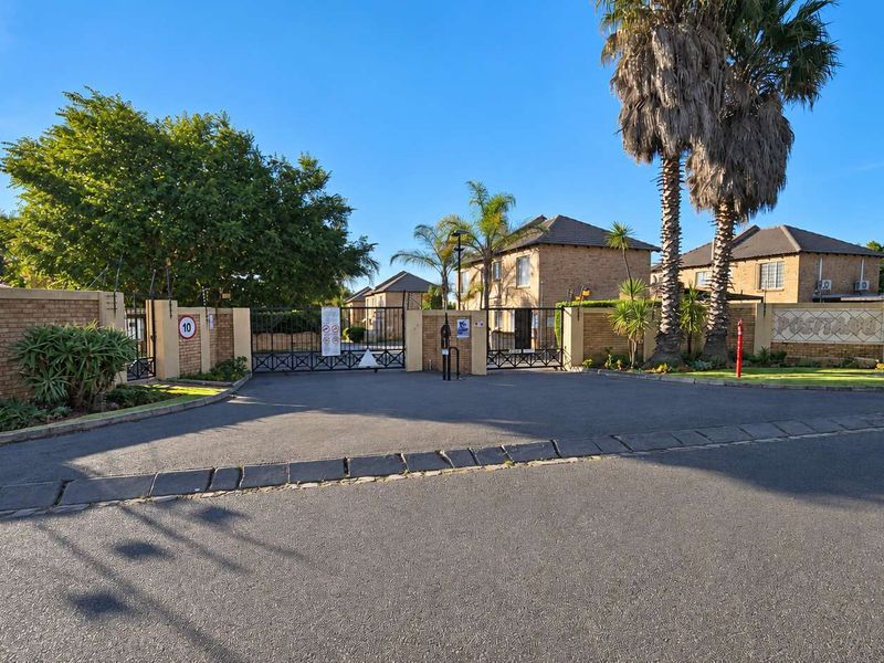 The entrance to the apartment complex features a secure gated access point with brick boundary walls and established landscaping.
