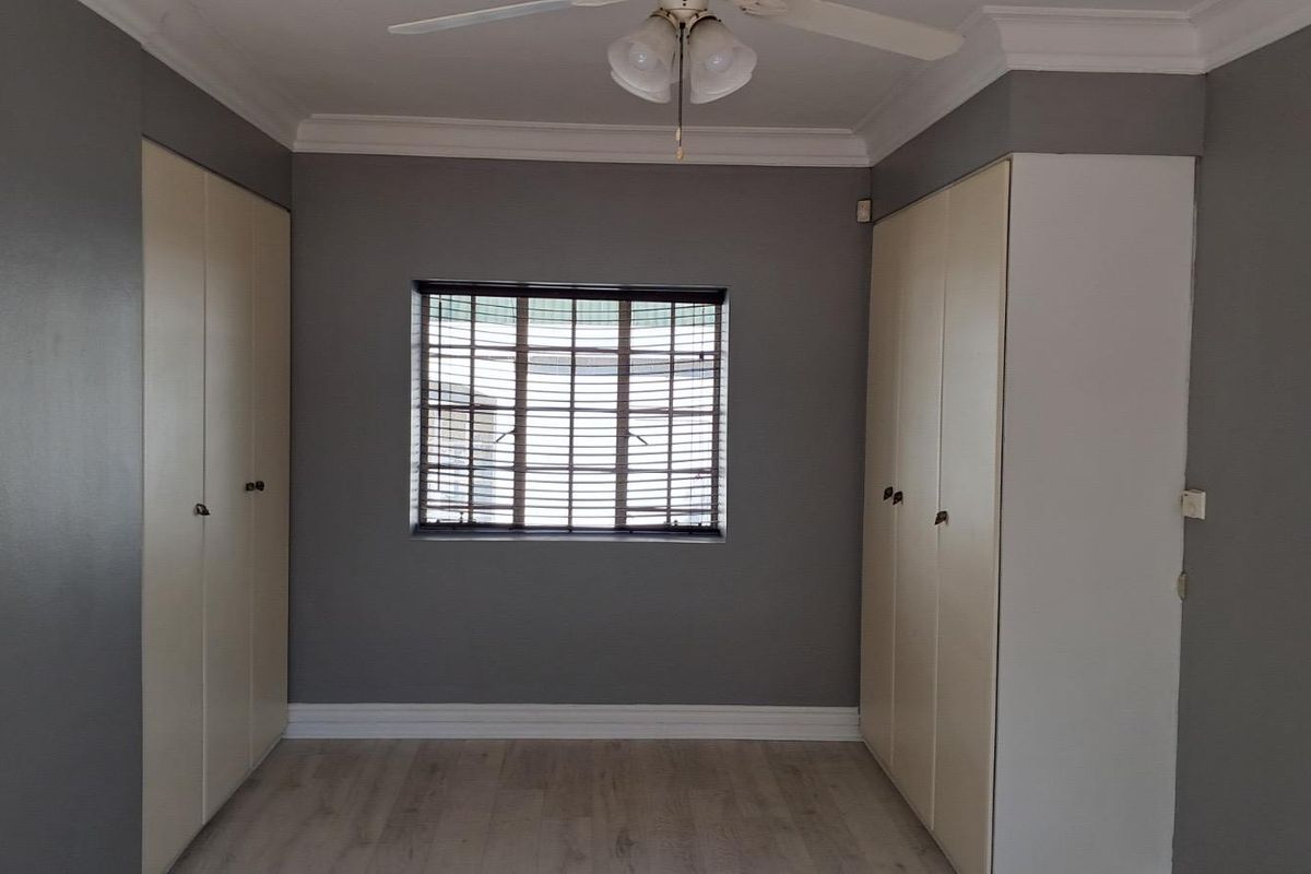 A well-maintained bedroom featuring built-in cupboards, laminate flooring, a ceiling fan, and a window with security bars.