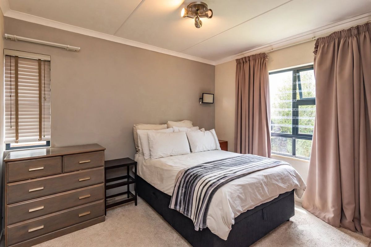 A well-maintained bedroom featuring neutral wall tones, carpeted flooring, and large windows with fitted blinds and curtains.