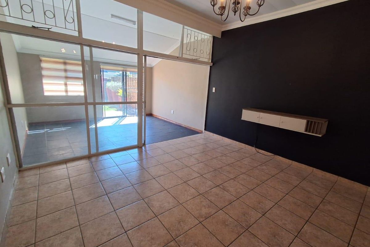 Spacious living area featuring tiled flooring, a built-in wall-mounted cabinet, and large glass sliding doors leading to an adjacent sunroom.