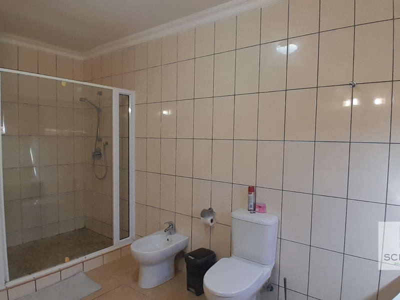 A functional bathroom featuring a glass-enclosed shower, bidet, and toilet with neutral wall tiling throughout.