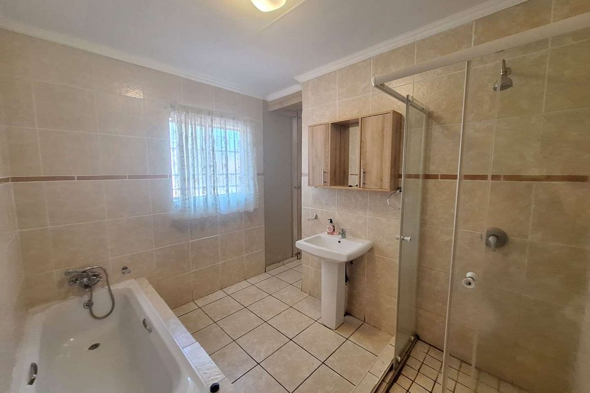 A functional bathroom featuring a pedestal basin, built-in bathtub, and a separate glass-enclosed shower with neutral ceramic tiling throughout.
