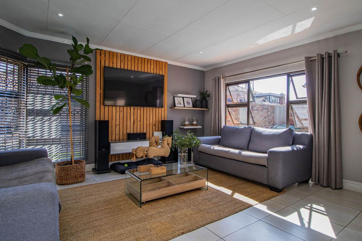 A well-maintained living room featuring a timber slat feature wall, tiled flooring, and large aluminium windows providing ample natural light.