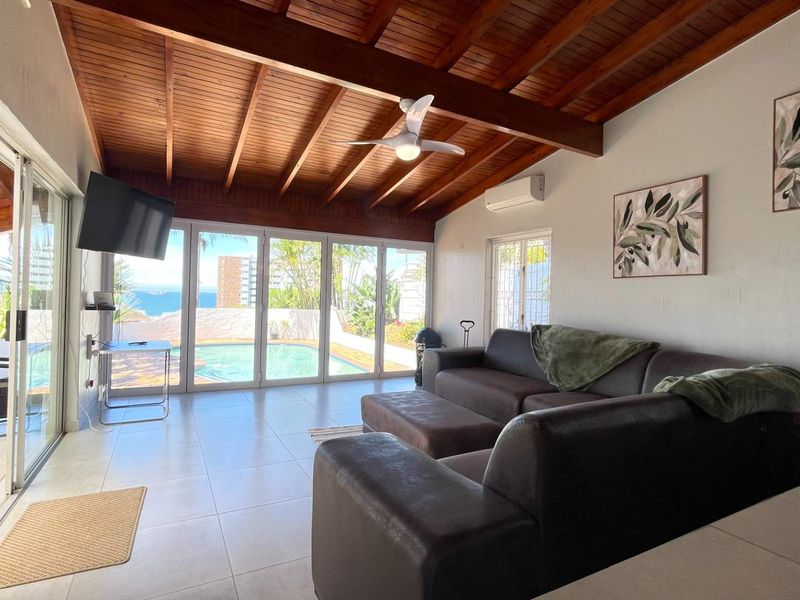 Spacious living area featuring an exposed timber beam ceiling, tiled flooring, and large sliding glass doors providing direct access to the pool area.