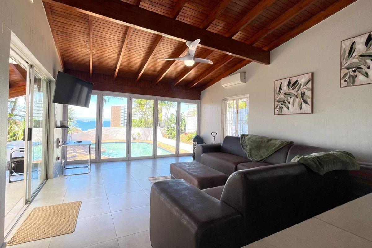 Spacious living area featuring an exposed timber beam ceiling, tiled flooring, and large sliding glass doors providing direct access to the pool area.