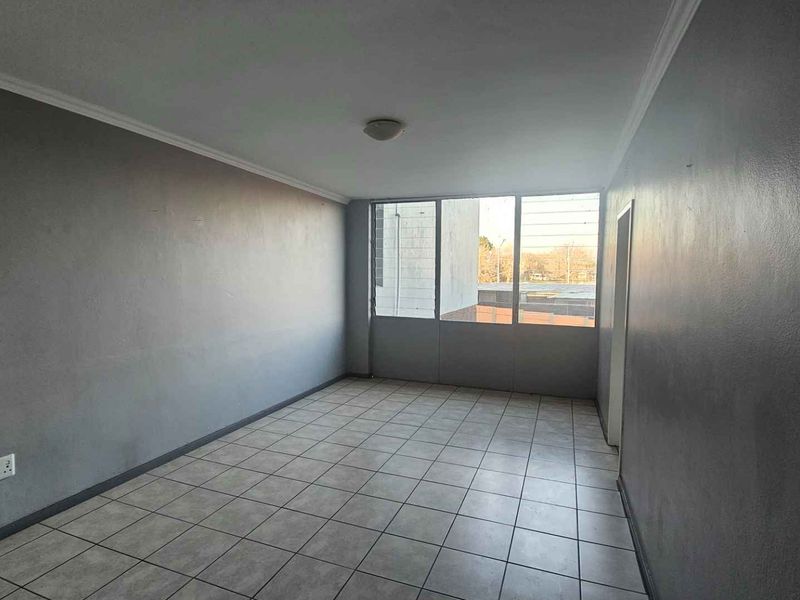 An empty living room featuring tiled flooring, grey painted walls, and large windows providing natural light.