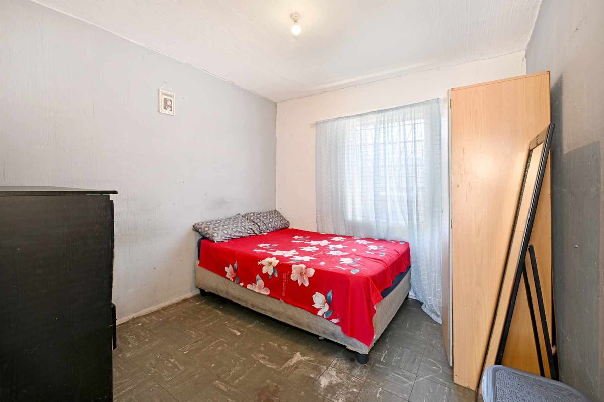 A bedroom featuring a window with security bars and worn flooring, offering a functional space ready for cosmetic updates and modernization.
