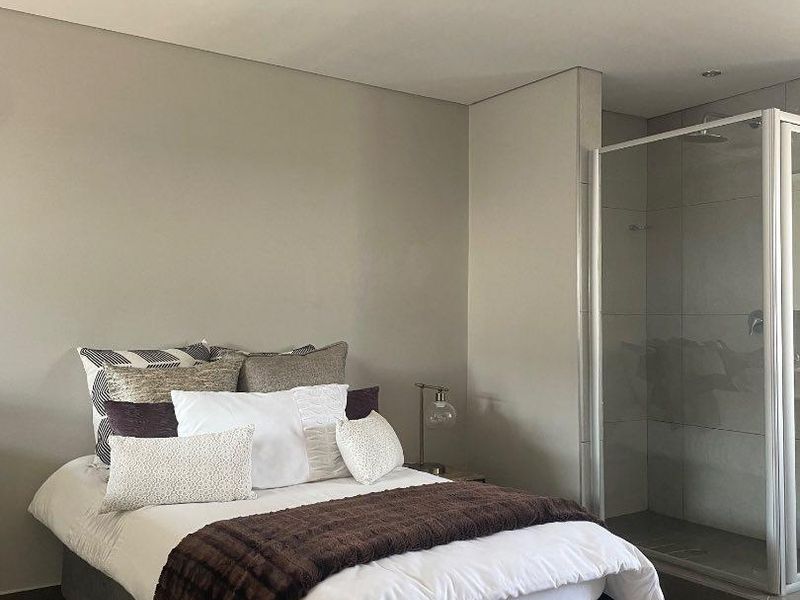 A modern bedroom featuring neutral wall tones, tiled flooring, and an integrated en-suite shower with a glass enclosure.
