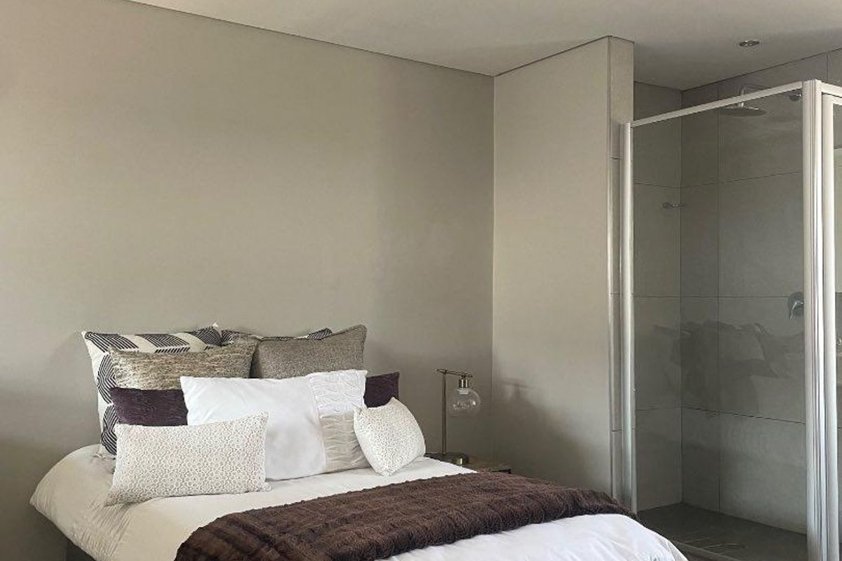 A modern bedroom featuring neutral wall tones, tiled flooring, and an integrated en-suite shower with a glass enclosure.