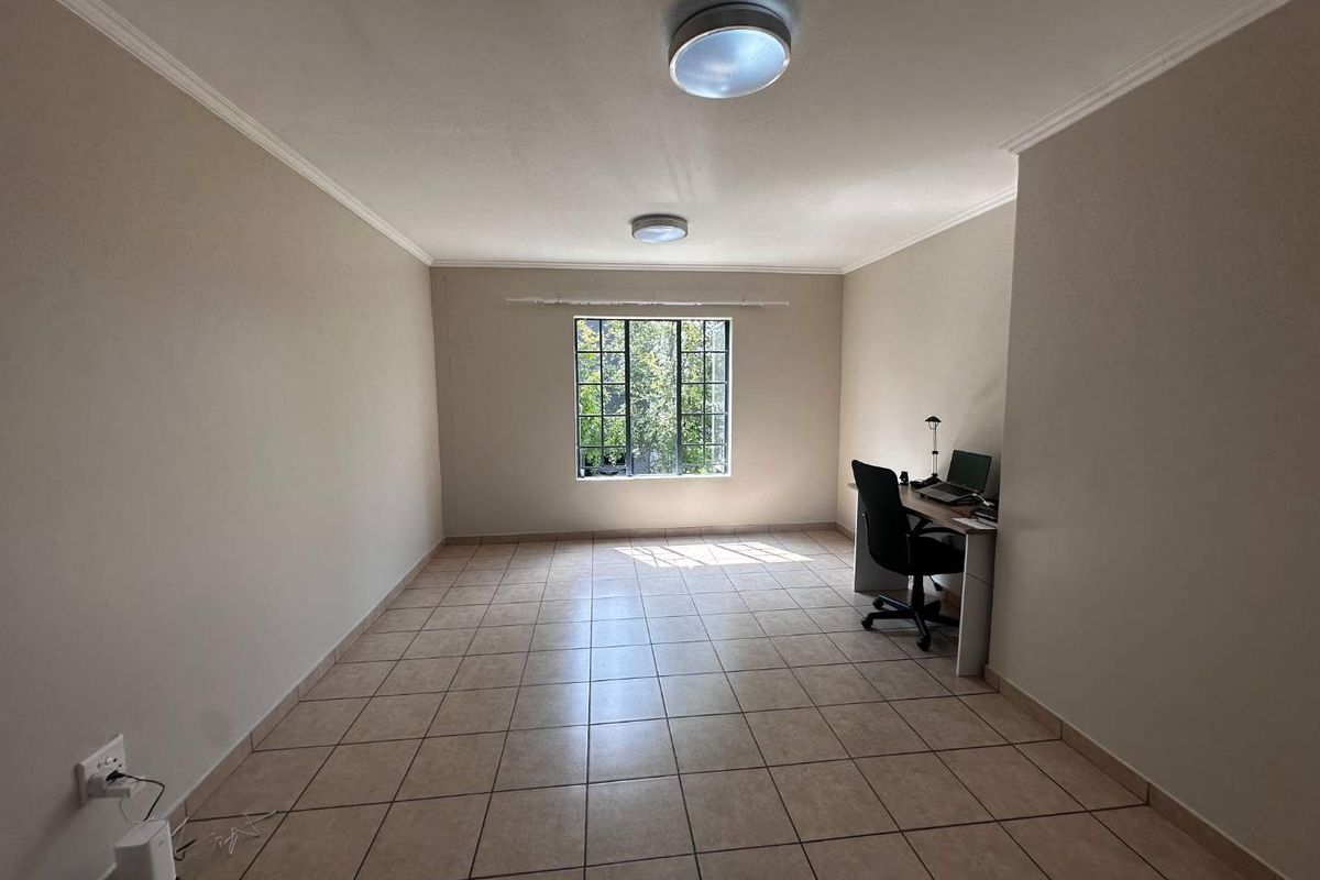 A spacious, neutrally painted room featuring tiled flooring, two ceiling-mounted light fixtures, and a window providing natural light.