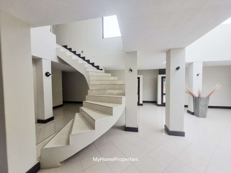 Spacious entrance hall featuring a striking curved staircase, neutral tiled flooring, and architectural columns, creating an open and bright welcoming area.