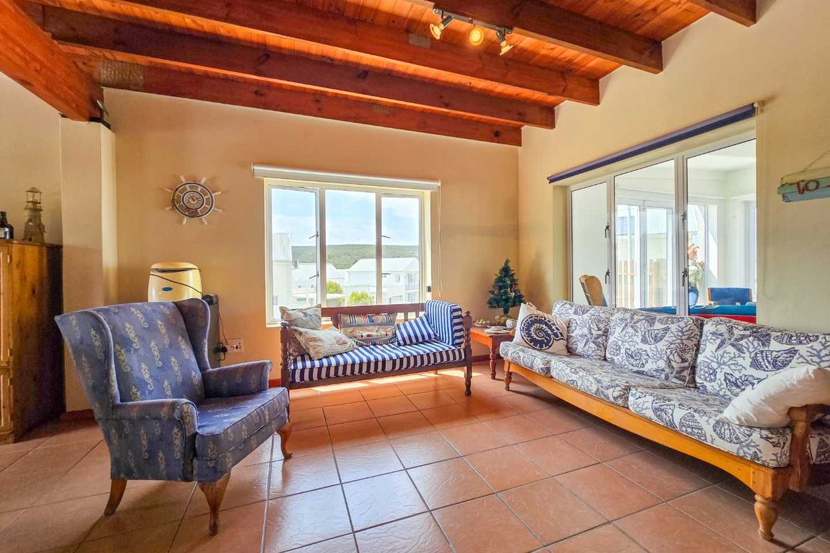Spacious living room featuring exposed timber ceiling beams, terracotta floor tiles, and large windows providing natural light and access to the outdoor area.