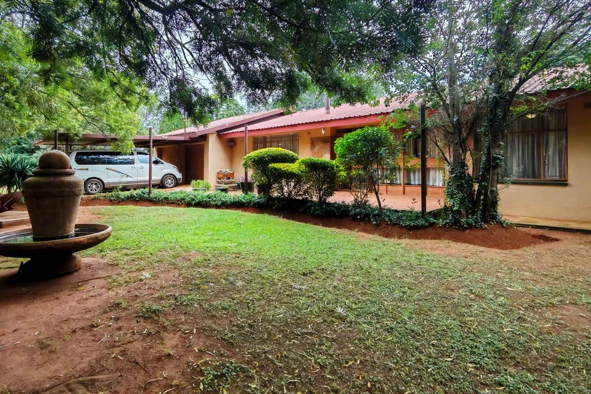 A view of the property's rear exterior, featuring a covered patio area, established garden, and a decorative stone water fountain.