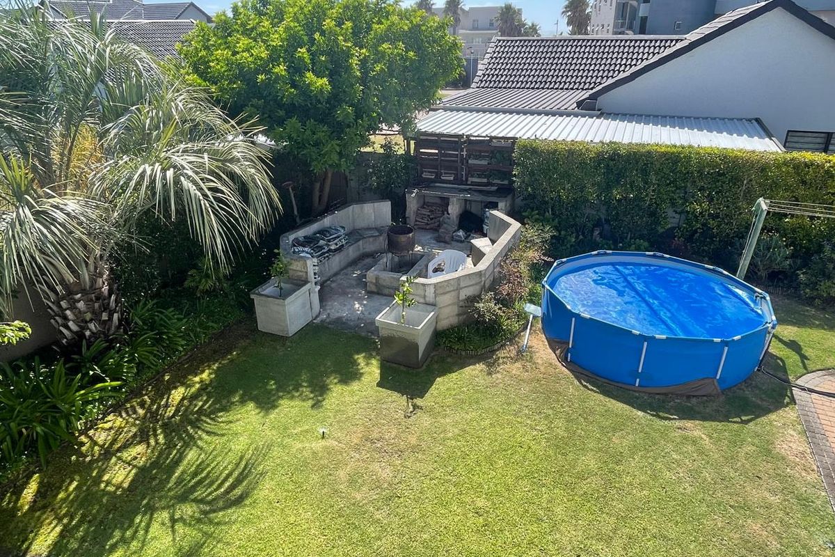 Elevated view of a rear garden featuring a built-in masonry braai area, established landscaping, and a portable above-ground swimming pool.