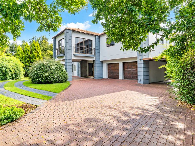 A well-maintained double-story residence featuring a paved driveway, double garage, and a balcony, set within a lush, landscaped garden.