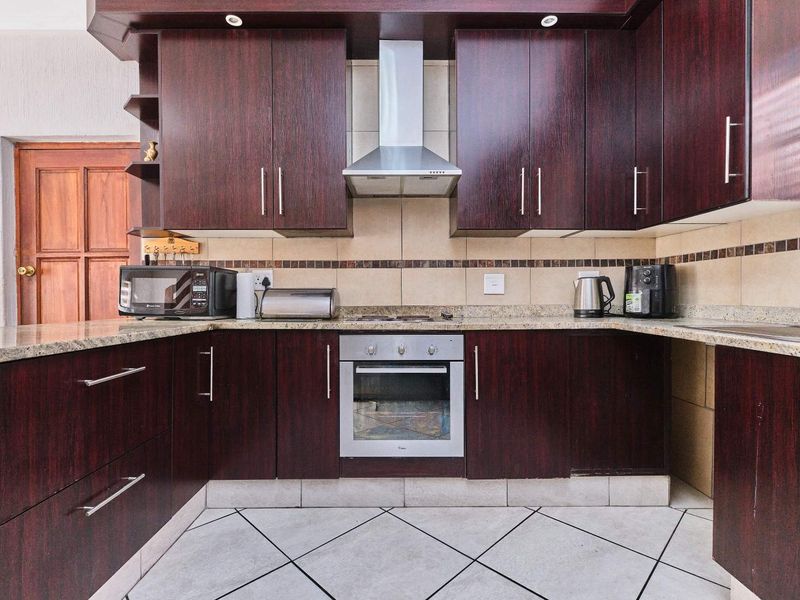 A functional kitchen featuring dark wood cabinetry, granite countertops, a built-in oven, and a stainless steel extractor fan with tiled flooring.