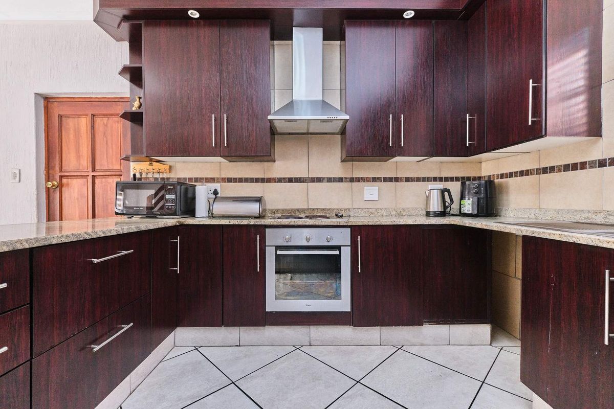 A functional kitchen featuring dark wood cabinetry, granite countertops, a built-in oven, and a stainless steel extractor fan with tiled flooring.