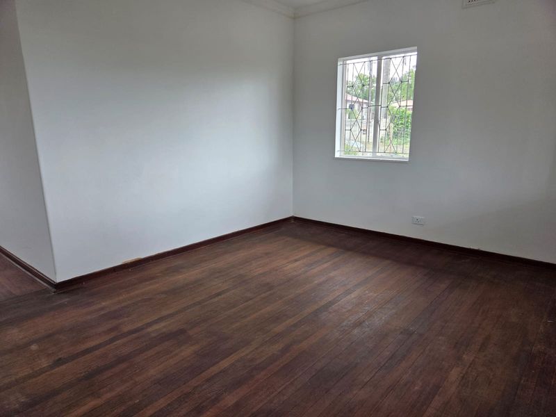 A vacant bedroom featuring original timber flooring, white walls, and a window fitted with security bars.