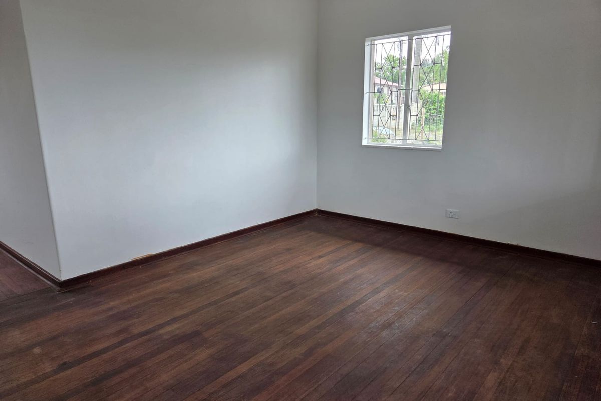A vacant bedroom featuring original timber flooring, white walls, and a window fitted with security bars.
