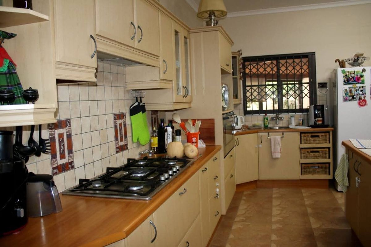 A functional kitchen featuring light-toned cabinetry, a gas hob, tiled backsplash, and a window with security bars.