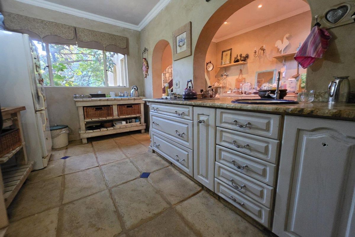 A rustic-style kitchen featuring stone floor tiles, arched wall openings, granite countertops, and traditional cabinetry with integrated sink and storage drawers.