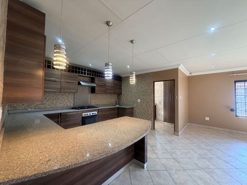 Modern kitchen featuring dark wood cabinetry, granite countertops, a gas hob, and tiled flooring, offering a functional and well-lit workspace.