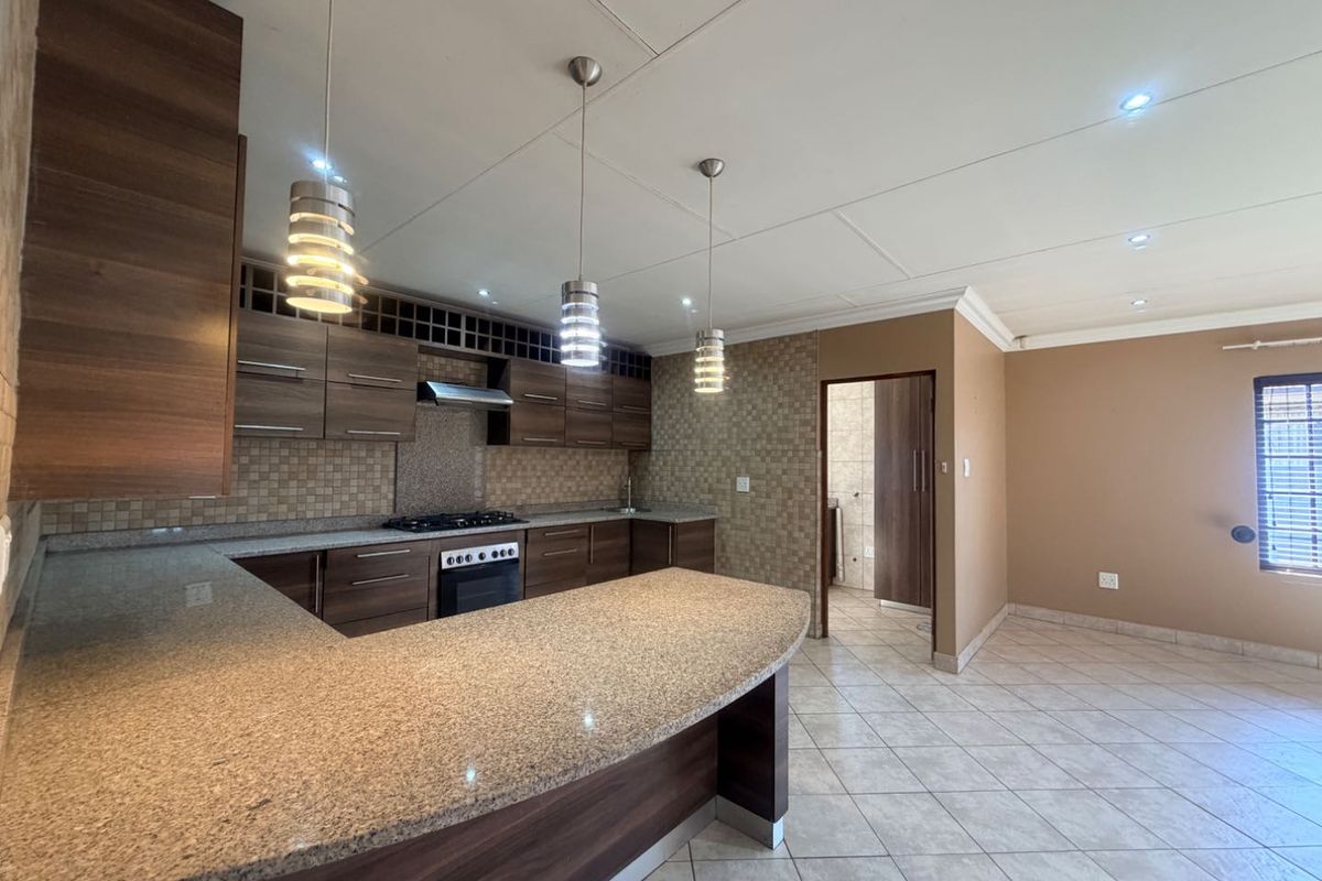 Modern kitchen featuring dark wood cabinetry, granite countertops, a gas hob, and tiled flooring, offering a functional and well-lit workspace.