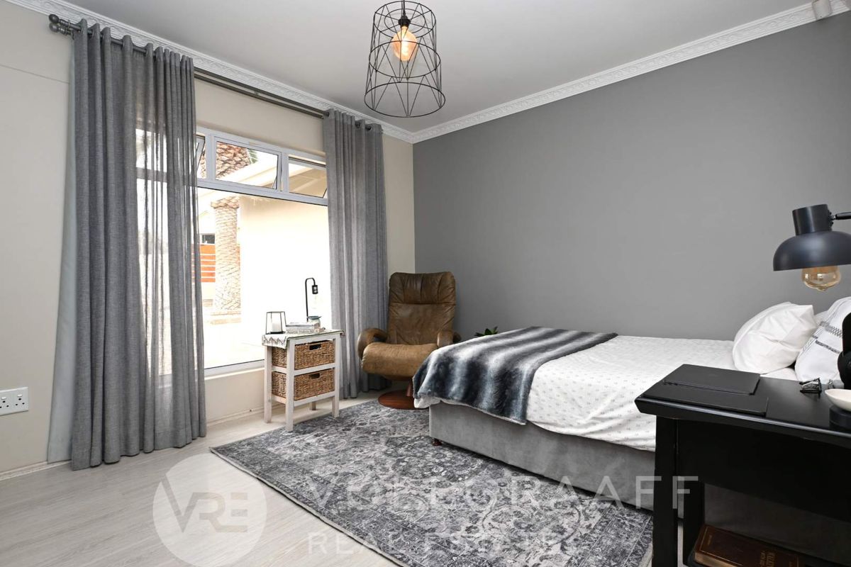 A well-maintained bedroom featuring neutral grey walls, decorative ceiling cornices, and large windows providing natural light.