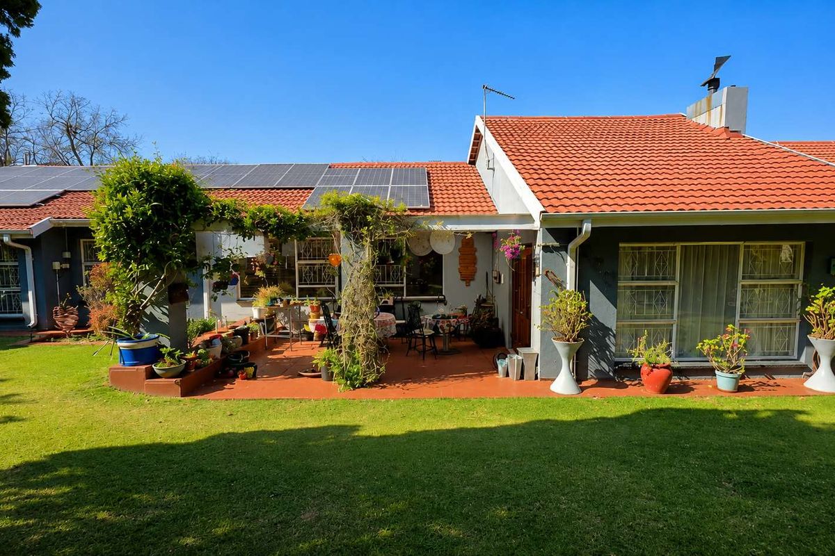 Rear view of the house featuring a covered patio, well-maintained lawn, and roof-mounted solar panels.