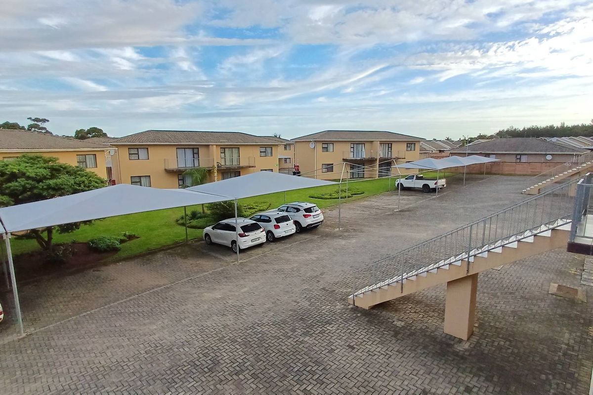 An elevated view of the apartment complex parking area featuring paved surfaces, shade-cloth carports, and landscaped garden spaces.