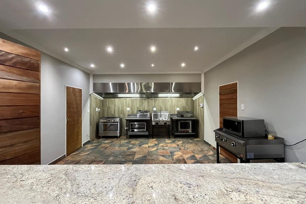 A professional-grade commercial kitchen featuring stainless steel appliances, a large extractor hood, stone-tiled flooring, and a granite-topped service counter.