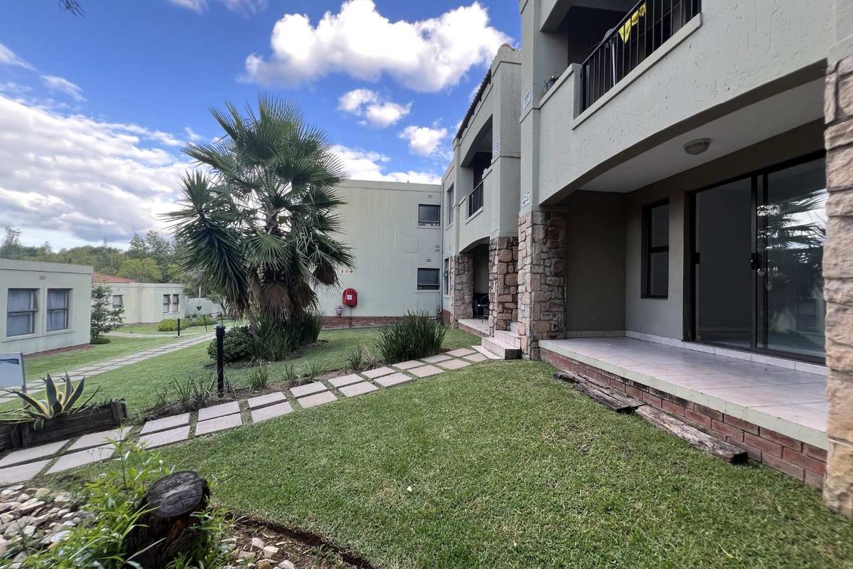 Exterior view of an apartment complex featuring a landscaped garden, paved walkways, and covered patio areas with stone pillar accents.