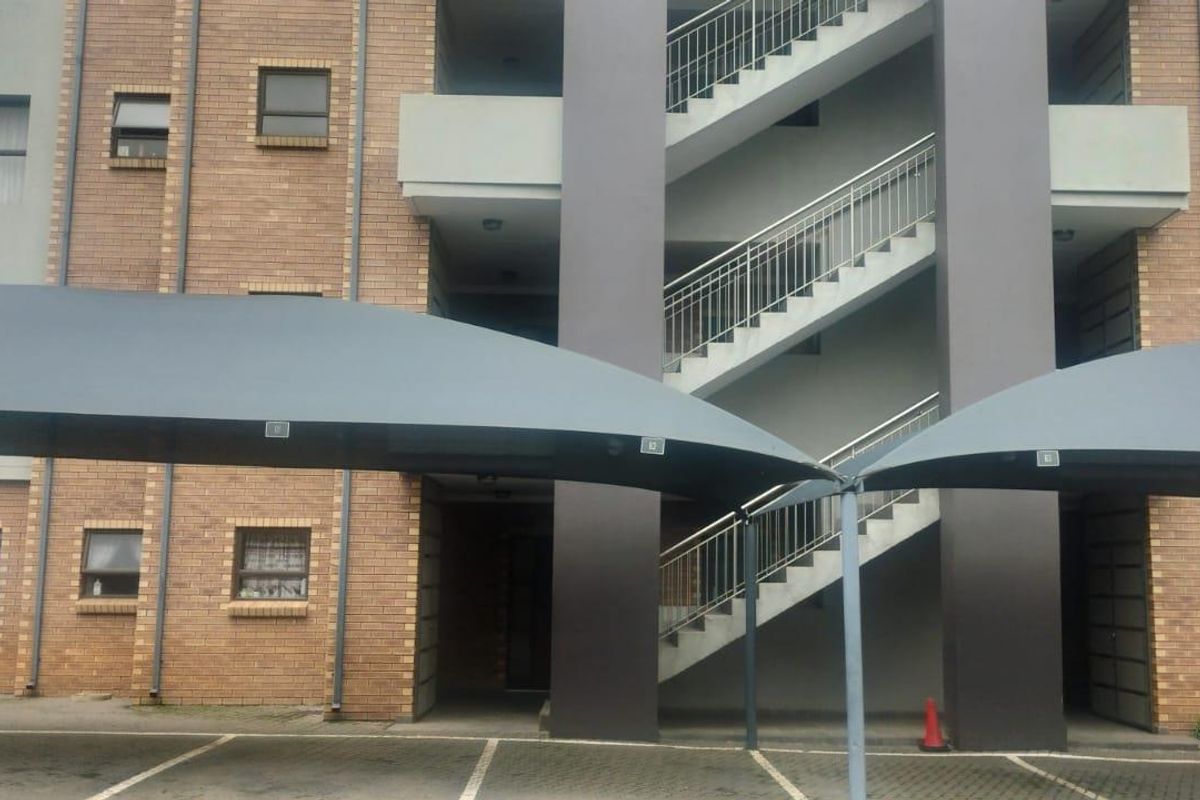 Front exterior view of a face brick townhouse complex featuring covered parking bays and an external staircase with metal railings.