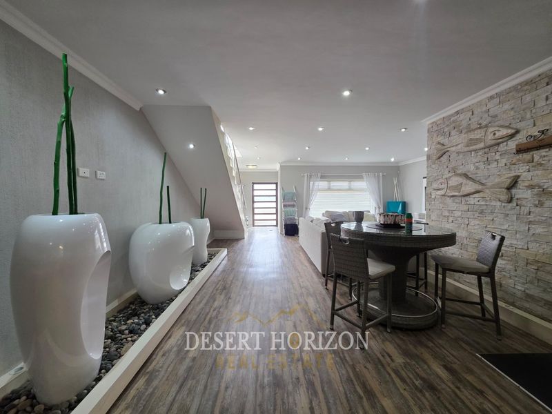 Spacious open-plan living area featuring a striking stone feature wall, modern recessed lighting, and durable laminate flooring with a unique pebble design element.
