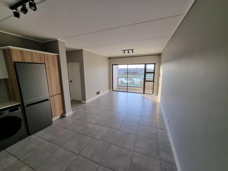 Open-plan living area featuring tiled floors, modern track lighting, and a sliding glass door leading to a balcony with scenic views.