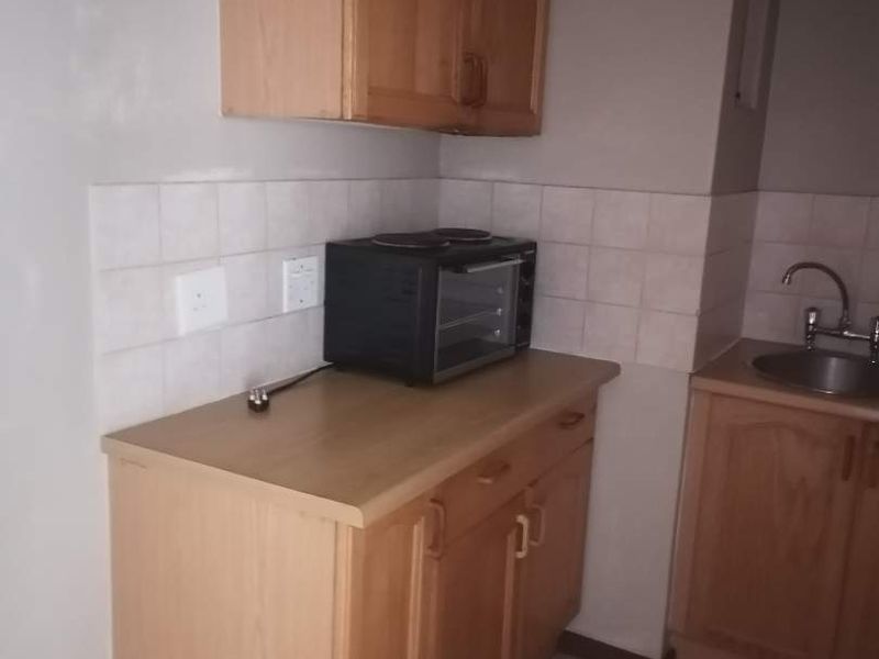 A functional kitchen area featuring wooden cabinetry, laminate countertops, a tiled backsplash, and a stainless steel sink with tiled flooring.