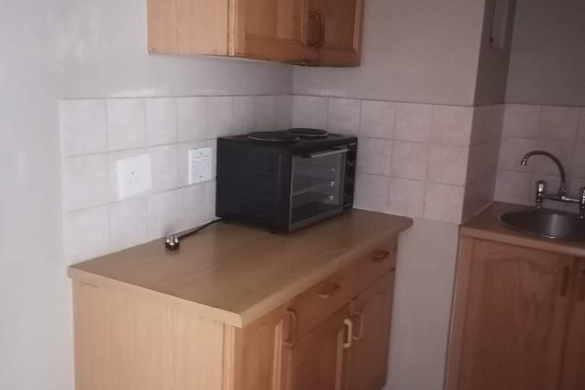A functional kitchen area featuring wooden cabinetry, laminate countertops, a tiled backsplash, and a stainless steel sink with tiled flooring.