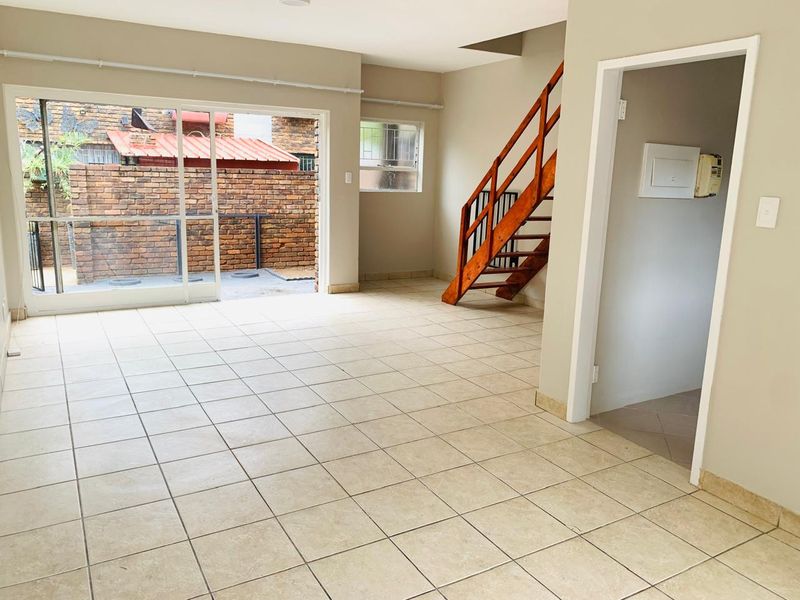 Spacious open-plan living area featuring neutral tiled flooring, a wooden staircase, and large sliding glass doors leading to an outdoor patio area.