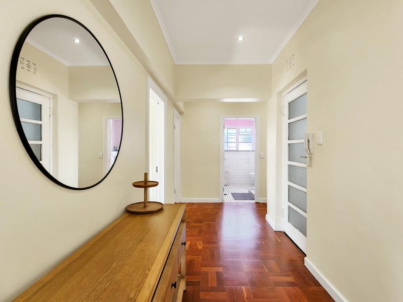 A bright and well-maintained hallway featuring warm parquet flooring, recessed lighting, and multiple internal doors leading to other areas of the apartment.