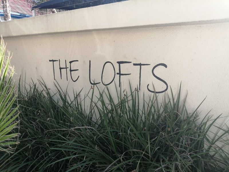 A view of the boundary wall at The Lofts apartment complex, featuring painted signage and landscaped greenery.