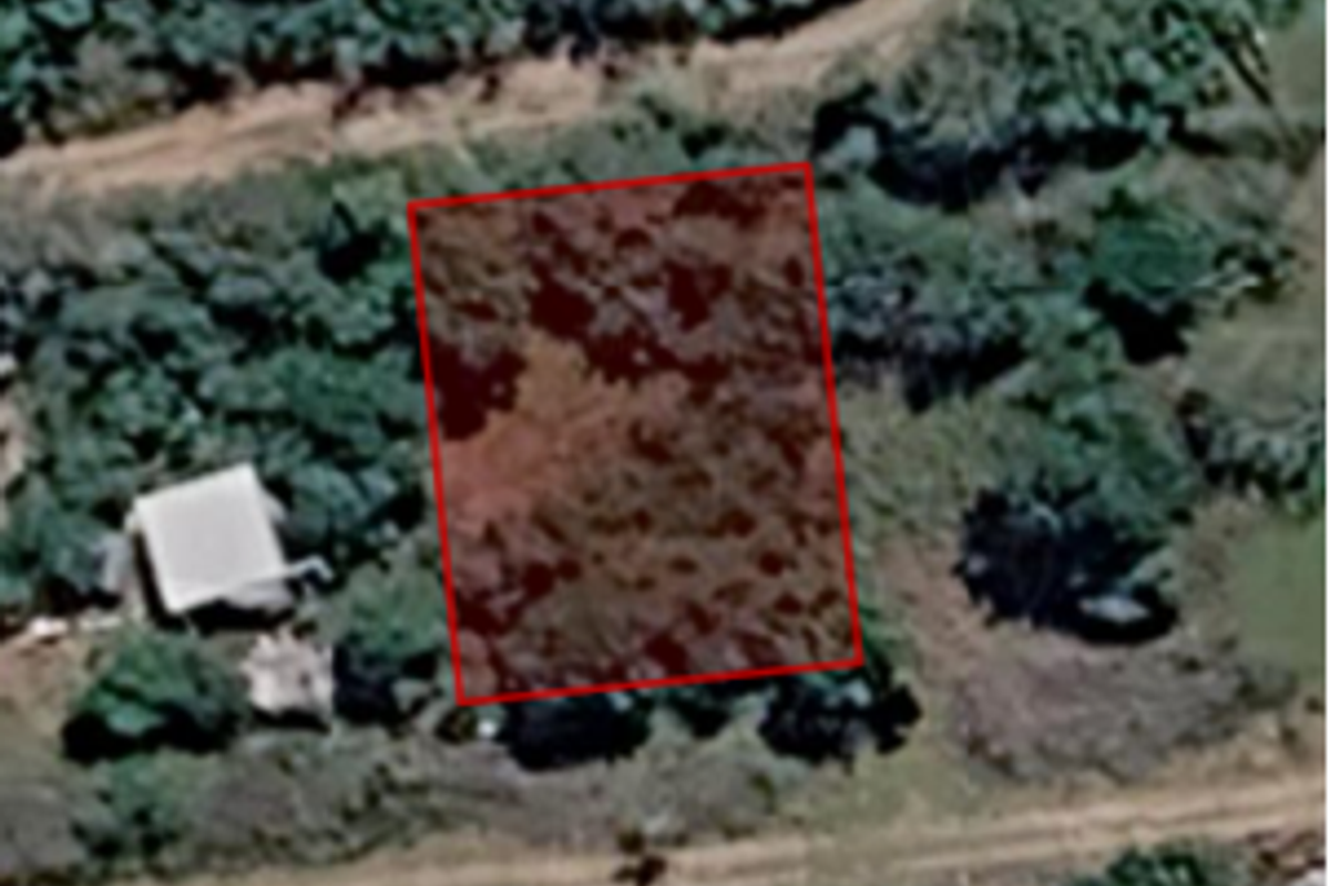 An aerial view of a vacant residential plot of land with surrounding vegetation.