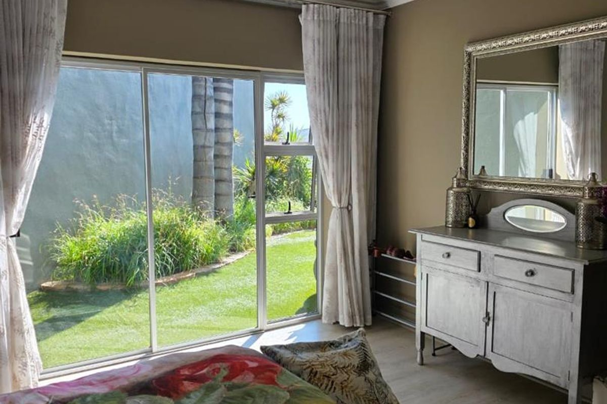 A bright bedroom featuring laminate flooring, recessed lighting, and a large sliding glass door providing direct access to the garden.
