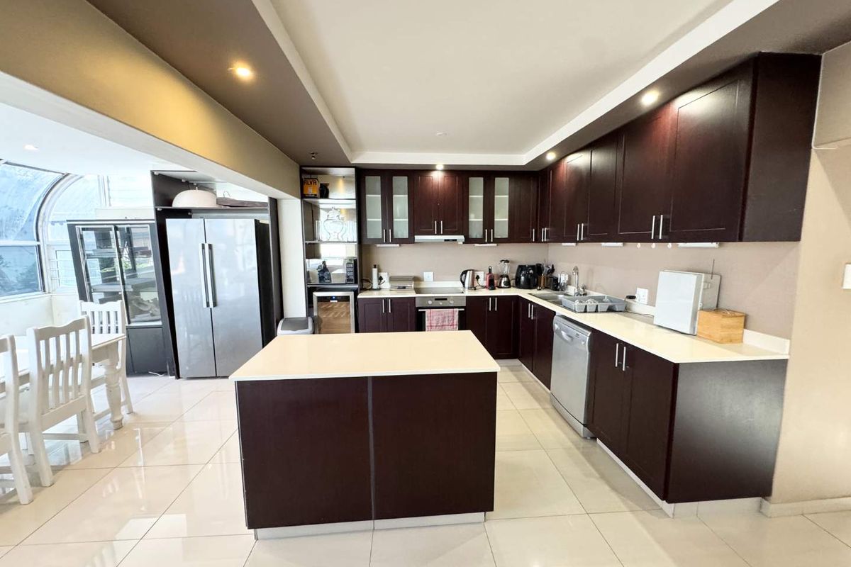 Modern kitchen featuring dark wood cabinetry, a central island with stone countertops, recessed lighting, and integrated appliances in an open-plan layout.