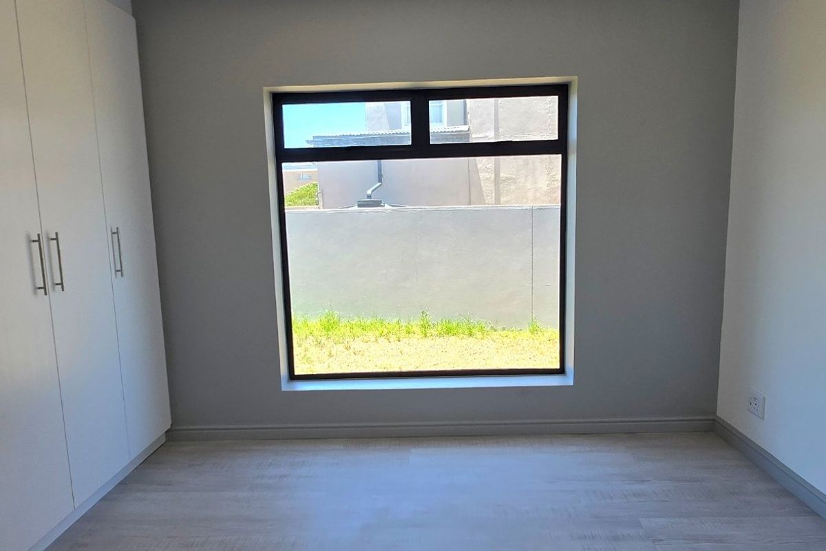 A bright, empty bedroom featuring modern laminate flooring and floor-to-ceiling built-in cupboards with a large window overlooking the rear garden area.